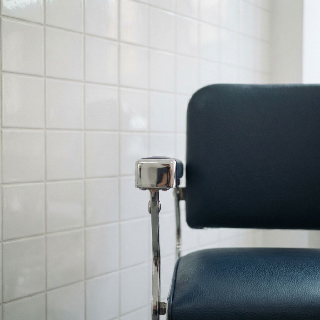 Detalle de un sillón de barbero cromado frente a la pared de azulejo blanco